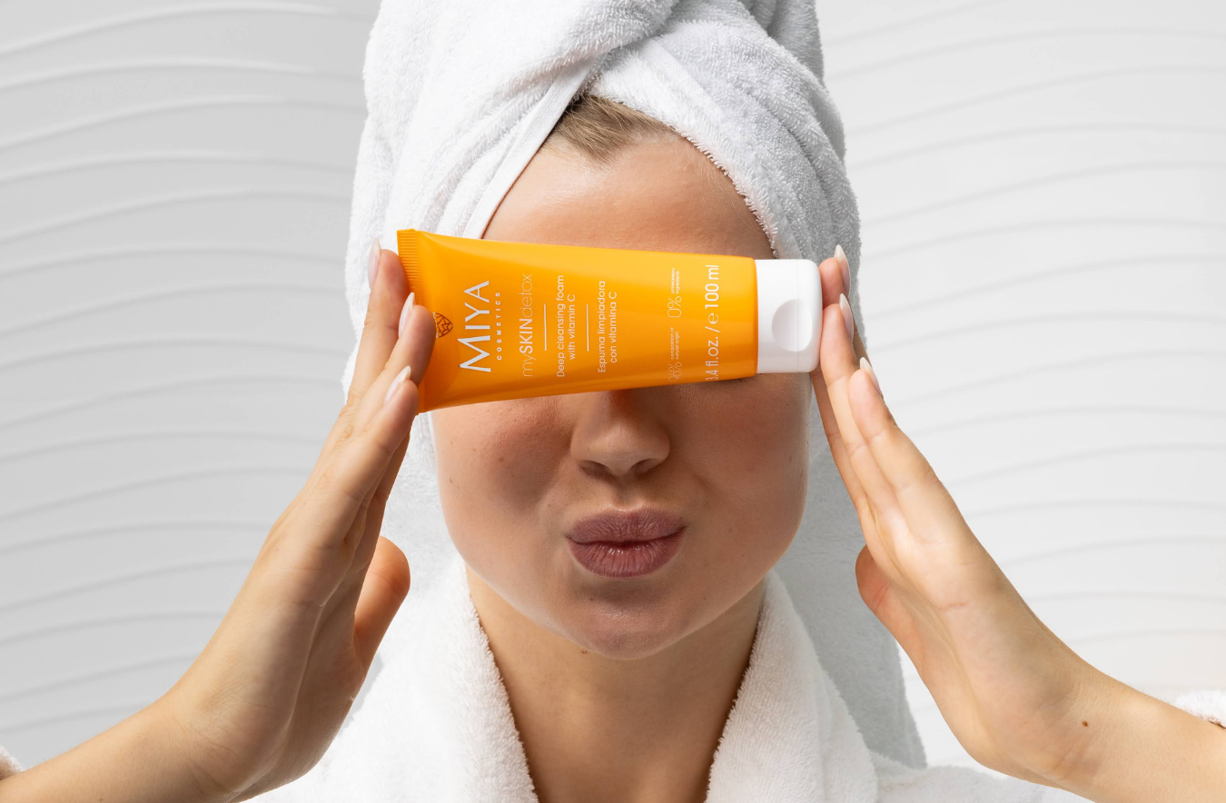 Person holding an orange tube labeled 'MIYA' near their face with a towel wrapped around their head.