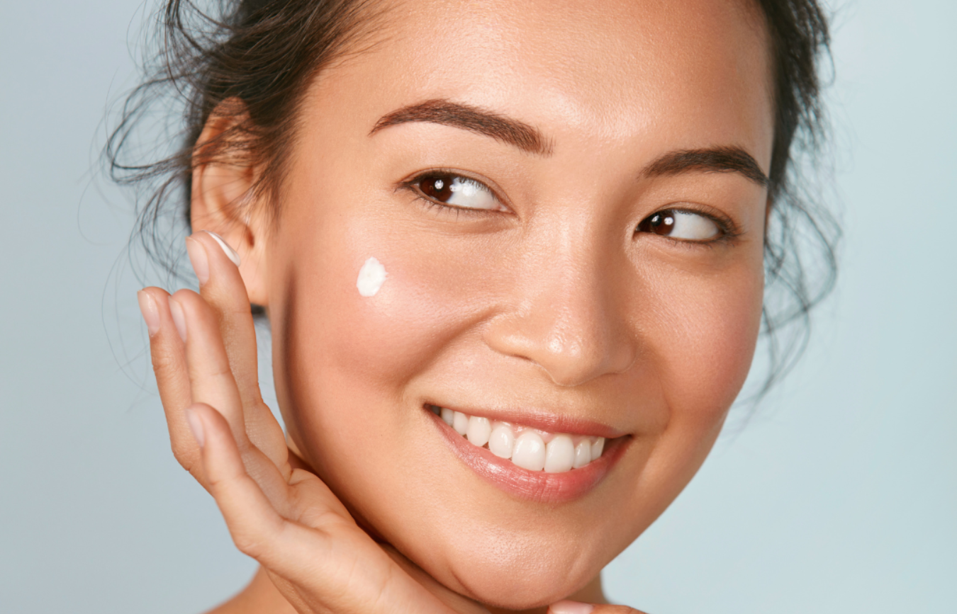 Woman applying cream to her face with a gray background