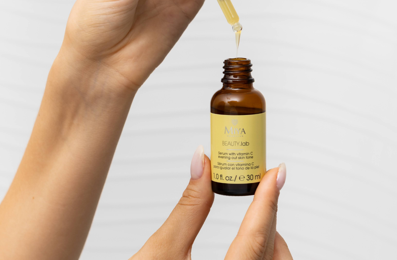 Hand holding a Natura Bissé dropper bottle with a droplet of liquid on a light gray background