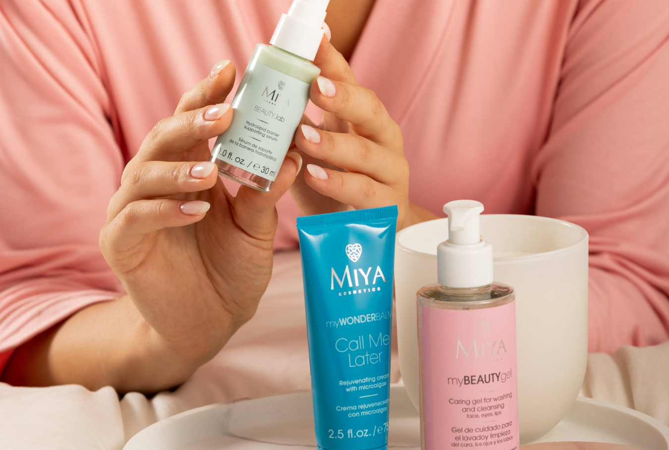 Person holding a skincare product with Miya Cosmetics bottles on a tray